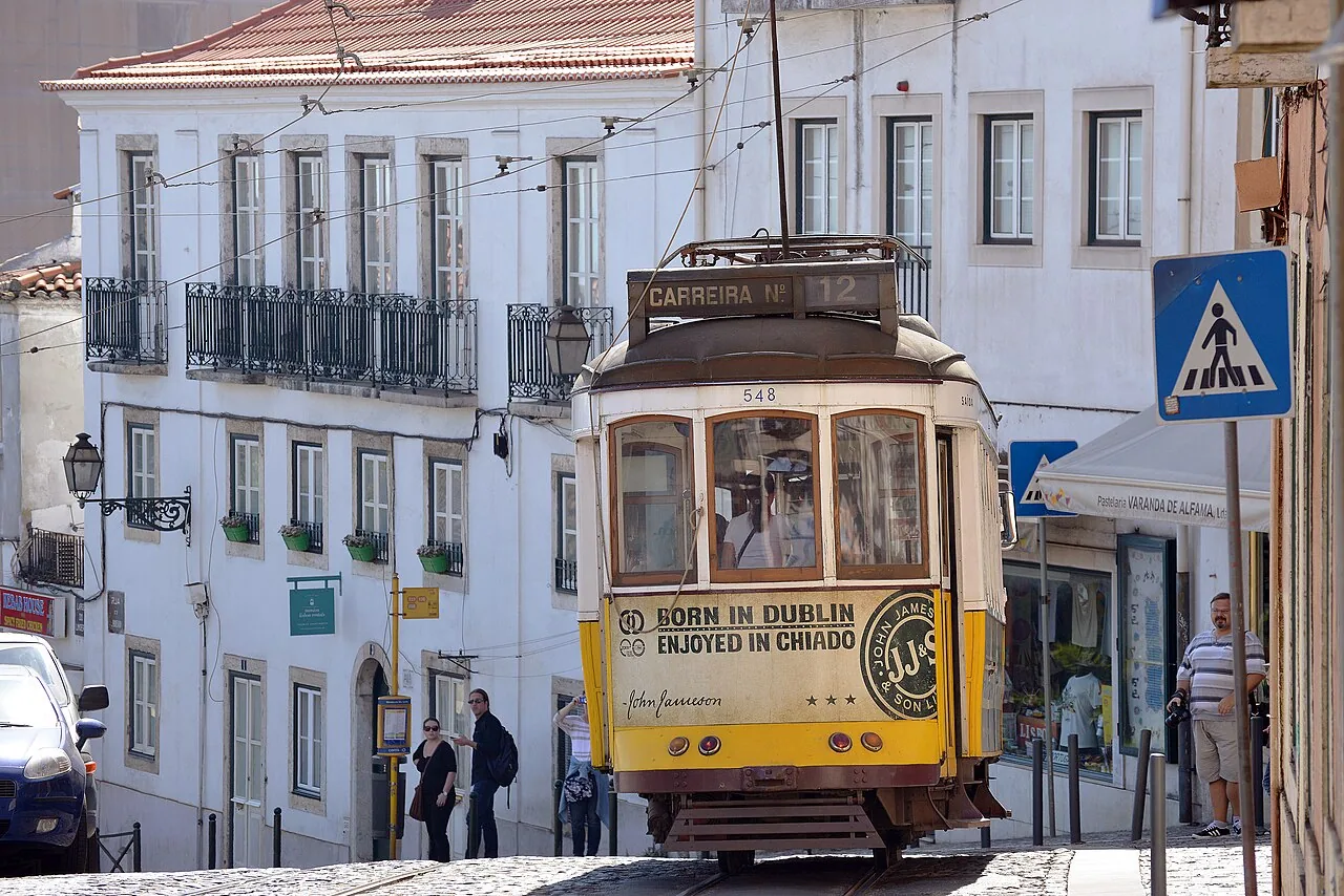 Yellow Lisbon tram on a street with pedestrians and pale facades